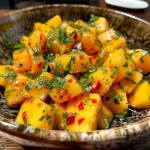 Naheinstellung eines bunten Mango-Gurken-Salats auf einem weißen Teller.