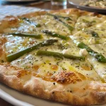 Nahaufnahme einer Pizza bianca mit Spargel auf einem Teller.