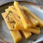 Nahaufnahme von knusprigen Polenta-Sticks auf einem Holzbrett.