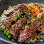 ['Close-up shot of a colorful steak fried rice dish featuring diced sirloin, vegetables, and garnished with green onions.', 'Side view of a bowl filled with stir-fried rice, juicy beef pieces, and vibrant vegetables.', 'Detailed image of Easy Steak Fried Rice showing cooked jasmine rice mixed with colorful ingredients and garnishes.', 'A close-up view highlighting the textures of fried rice with steak, peas, and carrots in a bowl.']