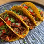 ['Close-up view of stuffed mini tacos with seasoned beef and vibrant toppings.', 'Side angle of delicious mini tacos filled with juicy ground beef and fresh vegetables.', 'A mouthwatering arrangement of mini tacos showcasing beef filling and colorful garnishes.', 'Close-up of mini tacos filled with spiced beef, topped with lettuce and tomatoes.']