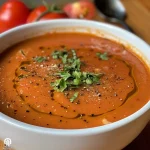 ['A close-up view of a bowl of vegan tomato soup, garnished with fresh basil and a sprinkle of red chili flakes.', 'A vibrant bowl of vegan tomato soup with pasta, topped with vegan parmesan and chopped herbs.', 'A rich, red tomato soup in a rustic bowl, featuring fresh ingredients like basil and a drizzle of plant cream.', 'A side view of creamy vegan tomato soup, showcasing its smooth texture and garnishes of parsley and chili flakes.']