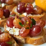 ['Close-up view of roasted grape bruschetta topped with whipped feta and orange zest.', 'Side view of bruschetta with juicy roasted grapes, creamy feta, and garnished with orange zest.', 'Appetizing bruschetta featuring roasted grapes and whipped feta on toasted baguette slices.', 'Delicious roasted grape and feta bruschetta displayed on a rustic wooden serving board.']