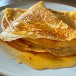 ['A close-up view of Crêpes au Potimarron, showcasing the rich orange filling and crispy edges.', 'A side angle photo of Crêpes au Potimarron, highlighting the golden-brown color and garnishes.', 'Detailed shot of Crêpes au Potimarron filled with pumpkin puree, topped with herbs and nuts.', 'Close-up image of a crêpe revealing its creamy pumpkin filling, sprinkled with chives and walnuts.']
