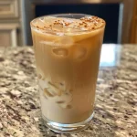 ['Close-up of a refreshing iced chai latte with a creamy texture and ice cubes.', 'Side view of an iced chai latte in a clear glass, showcasing its layered appearance.', 'Iced chai latte with a pinch of spice on top, served in a stylish glass.', 'A delicious iced chai latte with visible chai spices and a frothy milk layer.']