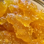 ['Close-up view of a jar of orange marmalade with a glossy finish, showcasing its vibrant orange color.', 'Side view of a container filled with homemade orange marmalade, highlighting its chunky texture.', 'Detailed shot of orange marmalade in a jar, reflecting light and emphasizing its rich, golden hue.', 'Close-up of a spoonful of orange marmalade, showing the zest and bits of orange peel throughout.']