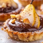 ['Close-up view of a Birnen-Haselnuss-Törtchen with a golden-brown crust and pear slices.', 'Side view of a delicious Birnen-Haselnuss-Törtchen showcasing its layered texture and glossy chocolate topping.', 'Rich Birnen-Haselnuss-Törtchen decorated with gold leaf, highlighting the chocolate and nut elements.', 'A detailed look at a Birnen-Haselnuss-Törtchen, emphasizing the pears and hazelnut filling.']