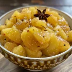 ['Close-up shot of a bowl of apple chutney with various spices nearby.', 'Side view of a vibrant apple chutney in a clear dish, garnished with spices.', 'Juicy apple chutney in a bowl, showcasing chunks of apple and spices.', 'A colorful presentation of apple chutney highlighting its texture and ingredients.']