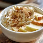 ['Close-up view of a creamy apple dip with apple slices.', 'Side view of a bowl of apple dip next to fresh apple slices.', 'Creamy dip in a bowl, garnished with apple slices for serving.', 'Apple dip made with cream cheese and brown sugar, served with apple slices.']
