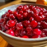 ['Close-up view of vibrant cranberry puree with sugared citrus fruits on top.', 'Juicy cranberry puree accompanied by glistening orange and lemon slices.', 'Side view of a thick cranberry puree garnished with sparkling citrus.', 'Rich red cranberry puree with slices of sugared orange and lemon.']