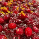 ['Close-up of a bowl of cranberry sauce with orange zest.', 'Side view of homemade cranberry sauce with orange juice and zest.', 'Juicy cranberry sauce in a decorative bowl, showcasing bright orange zest.', 'Fresh cranberry sauce with visible orange pulp and zest on a wooden surface.']