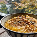 ['Close-up view of a creamy golden pumpkin porridge topped with pumpkin seeds and pecans.', 'Side view of a bowl of golden pumpkin porridge with a rich texture and garnished with nuts.', 'Mouthwatering golden pumpkin oatmeal in a bowl, featuring a sprinkle of seeds and nuts.', 'Delicious pumpkin porridge displayed in a bowl, highlighting its creamy consistency and toppings.']