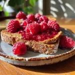 ['A close-up view of a slice of bread topped with almond butter, raspberry jam, and fresh raspberries.', 'A side perspective of a delicious toast with almond butter and vibrant raspberry toppings on a wooden surface.', 'A detailed close-up of raspberry almond butter toast featuring fresh fruit and spread on artisan bread.', 'A side shot of a gourmet toast showcasing creamy almond butter and ripe raspberries on crispy bread.']