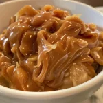 ['Close-up view of creamy caramel apple dip in a bowl, with fresh apples nearby.', 'Side profile of a bowl filled with caramel apple dip, with apple slices arranged around it.', 'Detailed shot of smooth caramel apple dip, featuring a spoon resting inside the bowl.', 'A vibrant presentation of caramel apple dip, showcased with whole apples for dipping.']