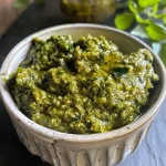 ['Close-up view of a jar filled with vibrant green Kürbiskernpesto.', 'Side angle of creamy Kürbiskernpesto with fresh herbs and pumpkin seeds.', 'Detailed shot of Kürbiskernpesto garnished with parsley and basil.', 'Close-up of a spoonful of Kürbiskernpesto showcasing its texture and color.']