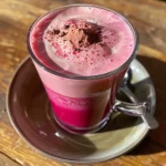 ['Close-up view of a pink latte with a frothy top, featuring beetroot powder, served in a clear glass.', 'Side view of a vibrant pink latte made with beetroot, showcasing its creamy texture and colors.', 'A refreshing pink latte in a glass cup, highlighting the rich beetroot color against a simple backdrop.', 'Detailed image of a pink beverage made with beetroot, emphasizing its creamy foam and enticing color.']