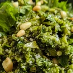 ['Close-up view of a bowl of Sellerie Pesto with vibrant green color and textured consistency.', 'Side view of creamy Sellerie Pesto made from celery leaves, showcased in a rustic bowl.', 'Freshly made Sellerie Pesto with visible pieces of celery leaves and pine nuts, served in a glass dish.', 'Juicy and rich Sellerie Pesto garnished with pine nuts and a drizzle of olive oil against a neutral background.']