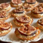 ['Close-up view of mini tartlets filled with goat cheese and topped with fresh figs.', 'Side view of almond shell tartlets showcasing creamy goat cheese and juicy figs.', 'Detail shot of bite-sized goat cheese and fig tartlets on a rustic wooden surface.', 'Beautifully arranged mini tartlets with golden almond crusts and fresh fig slices.']