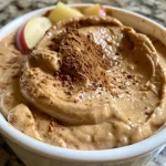 ['Close-up view of a creamy cinnamon almond butter dip with sliced green apples.', 'Side view of a bowl filled with cinnamon almond butter dip accompanied by apple slices.', 'Delicious almond butter dip garnished with cinnamon, served with fresh Granny Smith apple wedges.', 'Rich and creamy almond butter dip in a bowl with several sliced apples ready to be dipped.']
